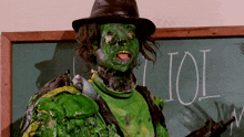 a person with green paint on their face stands in front of a blackboard that says ioi