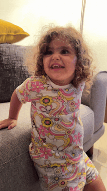 a little girl is sitting on a couch wearing a floral shirt