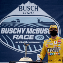 a man wearing a mask holds a m & m 's can in front of a busch light logo