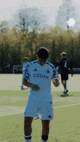 a soccer player wearing a white codan jersey stands on a field