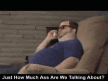a man sitting on a couch talking on a cell phone with the words just how much ass are we talking about below him