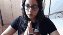 a girl wearing glasses and headphones praying with her hands folded