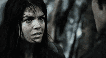 a woman with blood on her face is standing next to a man in the woods .