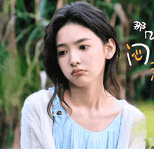 a woman in a blue top and white cardigan is looking at the camera