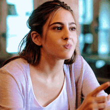 a woman wearing a white shirt and a purple cardigan is sitting at a table