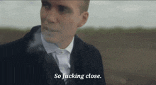a man in a suit is smoking a cigarette and saying so fucking close