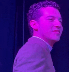 a man in a suit is standing in front of a purple light and smiling .