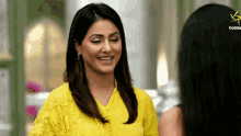 a woman in a yellow dress is smiling next to another woman with a hotstar logo in the background