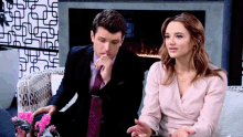 a man in a suit and tie sits next to a woman in a pink top