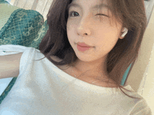 a woman wearing a white shirt and earbuds winks at the camera