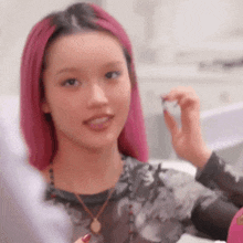 a young woman with pink hair is sitting at a table holding a small object .