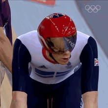 a british athlete wearing a red helmet and goggles with the olympic rings in the background
