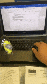 a person is typing on a laptop with a yellow bird on the keyboard