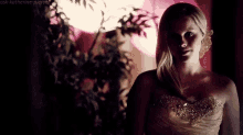 a woman in a strapless dress is standing in a dark room looking at the camera .