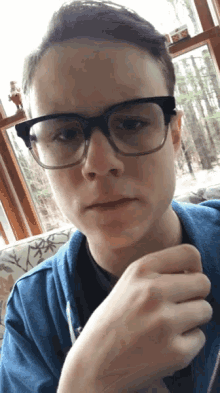 a young man wearing glasses and a blue sweatshirt looks at the camera