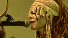 a woman with dreadlocks singing into a microphone with fringe on her head