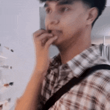 a man in a plaid shirt is biting his nails while standing in front of a refrigerator .