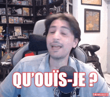 a man sitting in front of a microphone with the words qu'ouis-je in red