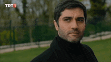 a man in a black turtleneck looks at the camera with trt1 written on the bottom of the screen