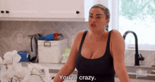 a woman in a black tank top says " you 're crazy " in a kitchen
