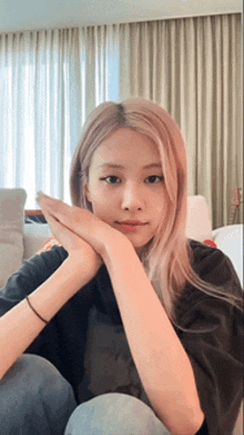 a woman with long blonde hair is sitting on a couch with her hands on her face