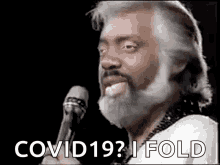 a man with a beard is singing into a microphone and says `` covid19 ? i fold '' .