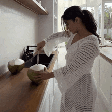 a woman in a white dress is opening a green coconut