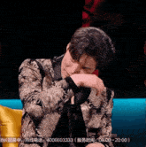 a man in a suit is sitting on a couch and covering his face