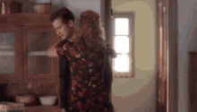 a man and a woman are dancing in a kitchen . the woman is wearing a floral dress .