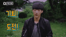 a young man in a black jacket stands in a field with chinese writing on the ground