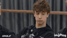 a young man in a black hoodie is sitting in front of a curtain with imgplay written on the bottom