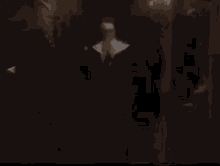 a nun is praying in a dark room while a man in a suit looks on .