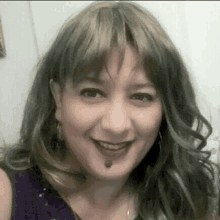 a woman wearing a purple top and earrings is smiling for the camera