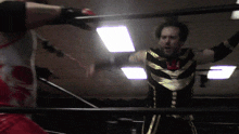 a man in a gold and black outfit is standing in a ring with his arms outstretched