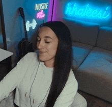 a woman sits in front of a neon sign that says hustle and grind