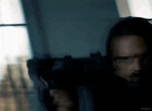 a man with a beard is holding a gun in front of a window in a dark room .