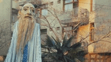 a statue of a man with a long beard is standing in front of a building in a city .