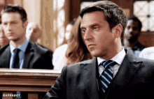 a man in a suit and tie sits in a courtroom with barbabot written on the bottom right