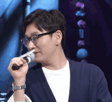 a man wearing glasses and a watch holds a microphone in his hand