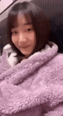 a woman is wrapped in a purple blanket and smiling at the camera .