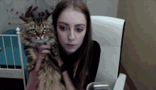a girl is holding a cat in her lap and looking at the camera