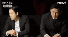 two men in suits are sitting next to each other in front of a banner that says mil12
