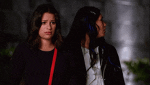 two women standing next to each other with one wearing a red purse