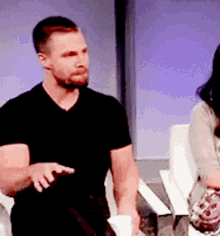 a man in a black shirt sits next to a woman in a chair