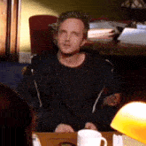 a man is sitting at a table with a cup of coffee in front of him .