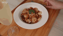 a bowl of shrimp sits on a wooden tray next to a wine glass