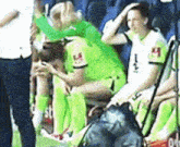 a group of soccer players are sitting on a bench with one wearing a white jersey with the letter h on it