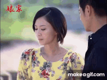 a man and a woman are standing next to each other and talking . the woman is wearing a yellow floral shirt .