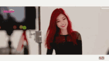 a woman with red hair is smiling in front of a camera .