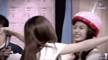 a woman wearing a pink helmet is hugging another woman wearing a white shirt .